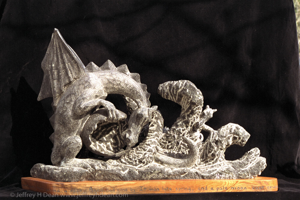 Stone carving of mother and baby dragon with the beginning of a story around the base.