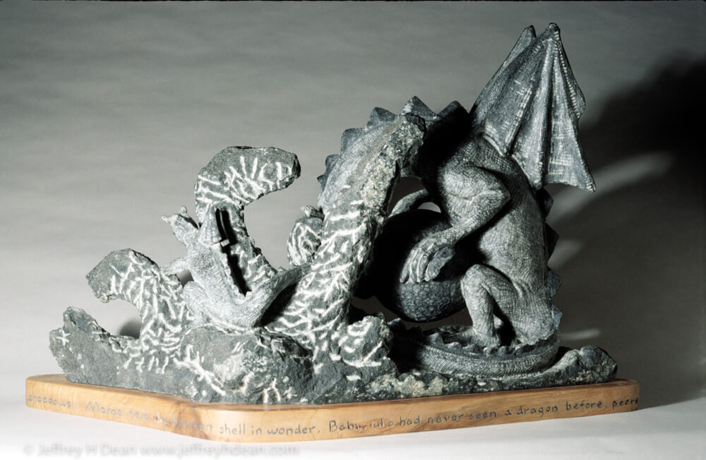 Stone carving of mother and baby dragon with the beginning of a story around the base.