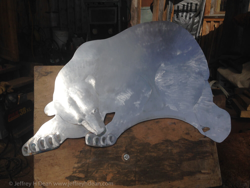 A lone polar bear and arctic fox watch silently as a seal rises to it's breathing hole in this layered steel and wood relief.