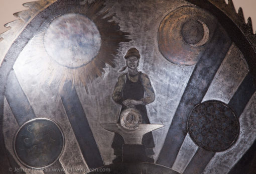 Earth, air, fire and water; the resources of the smith. Engraved steel sawblade of blacksmith in the forge.