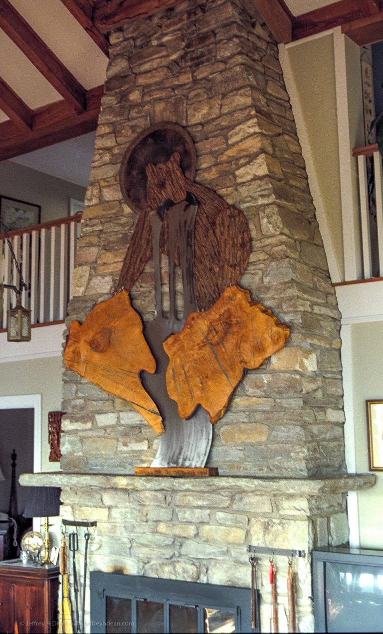 Large wood and metal wall art of a fishing bear with the sun shining from behind on rock chimney wall.