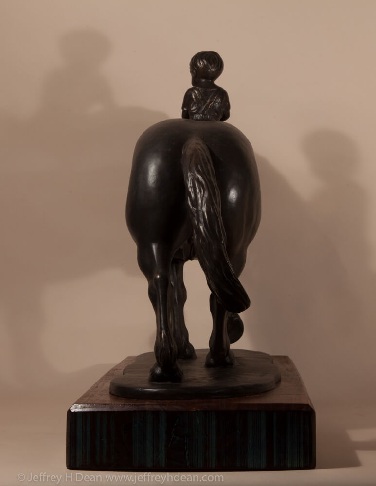 Bronze sculpture of a young boy riding a draft horse.
