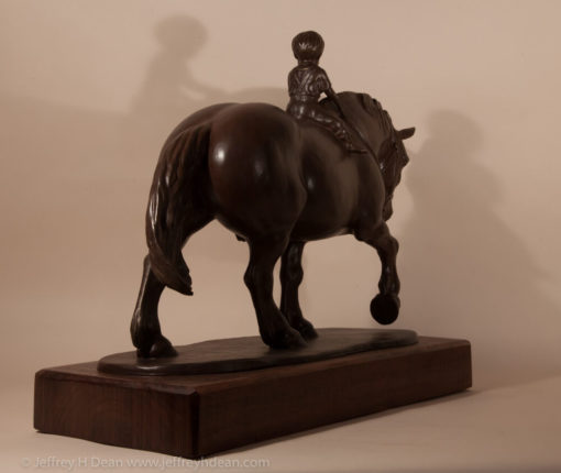 Bronze sculpture of a young boy riding a draft horse.
