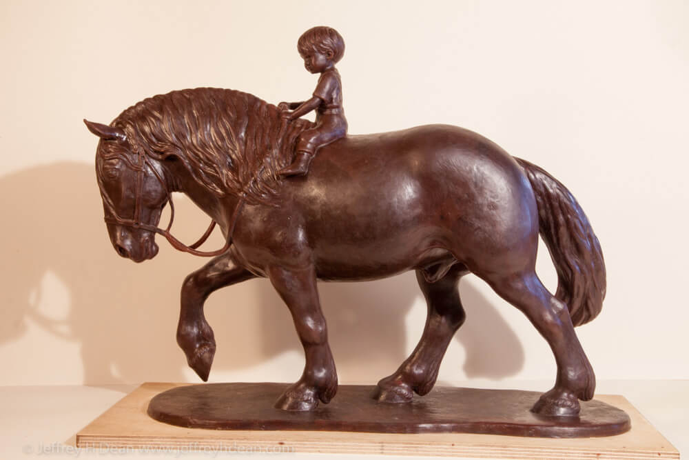 Wax model of a young boy riding a draft horse.