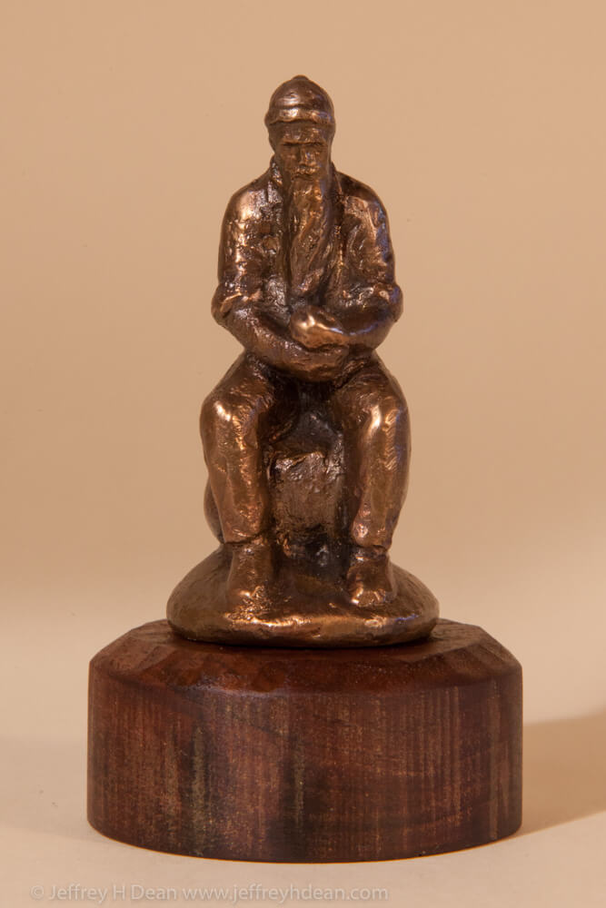 Miniature bronze sculpture of old timer sitting on a rock eating an apple.