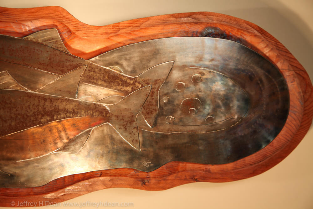 Three salmon rest in the shallow headwaters of a northern stream bed. Engraved steel wall relief.