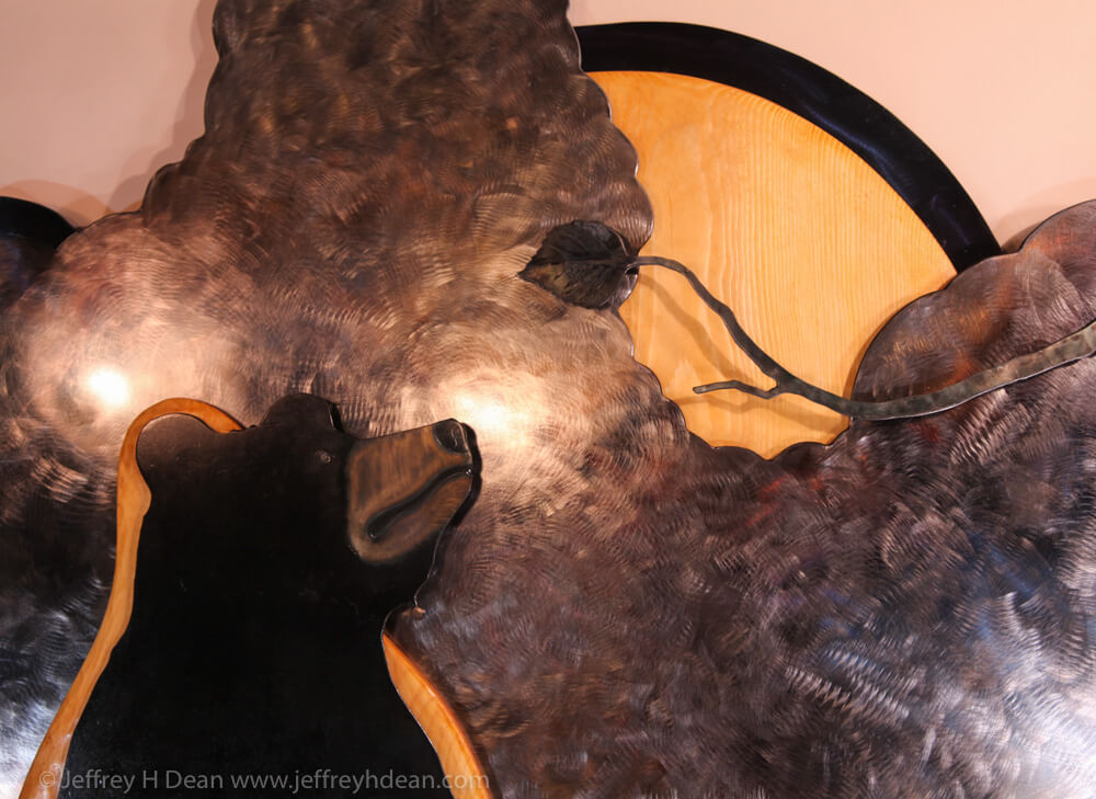 Layered steel and wood wall art of a fishing black bear, a salmon, a raven in a birch tree.